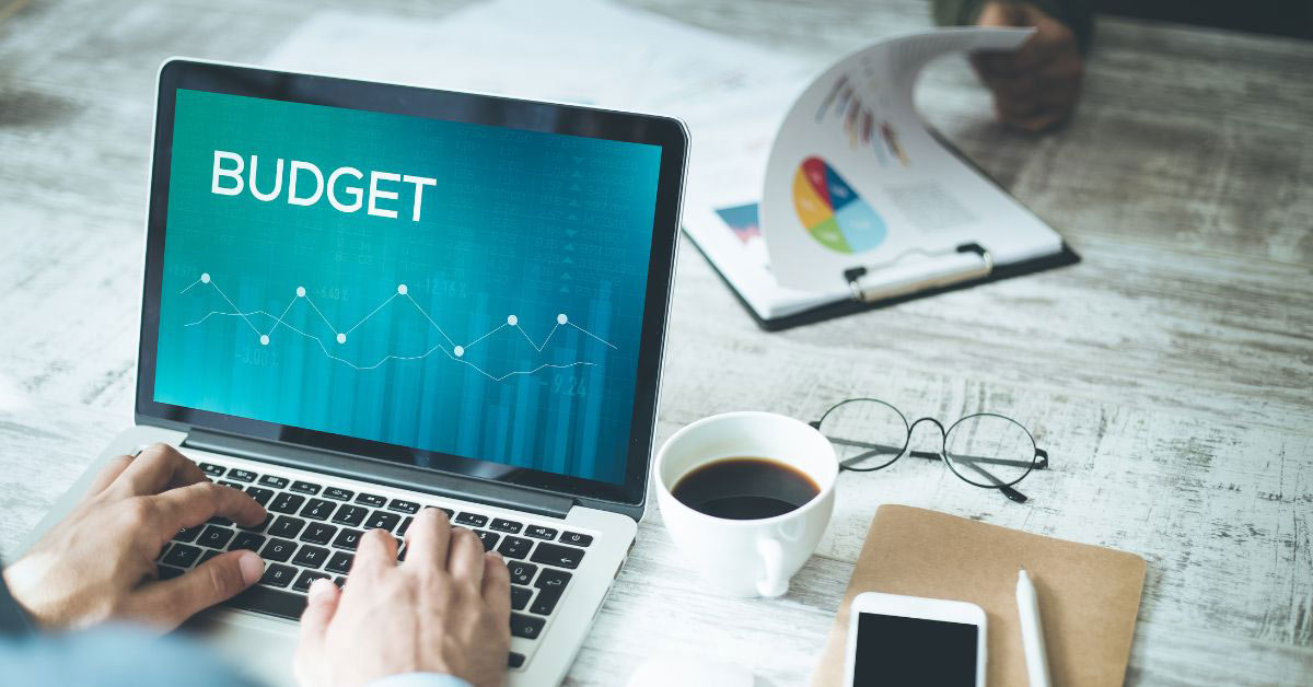 Image of a desk with devices and coffee and a laptop that says 'Budget'