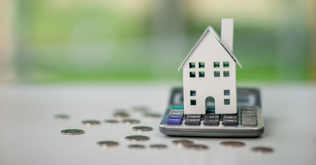 Image of a toy house on top of a calculator with coins below it