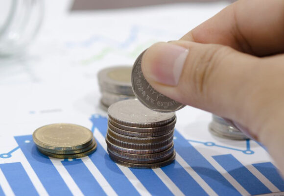 Image of a hand stacking quarters, over a piece of paper with financial charts