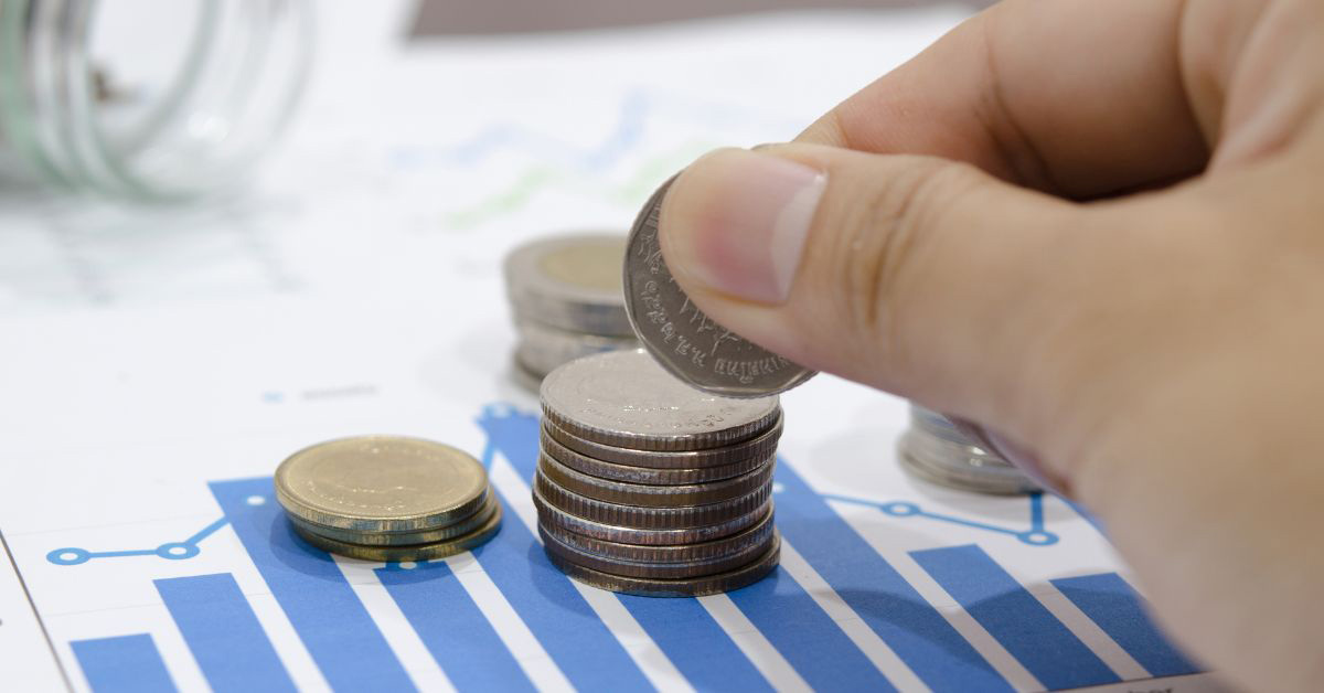 Image of a hand stacking quarters, over a piece of paper with financial charts