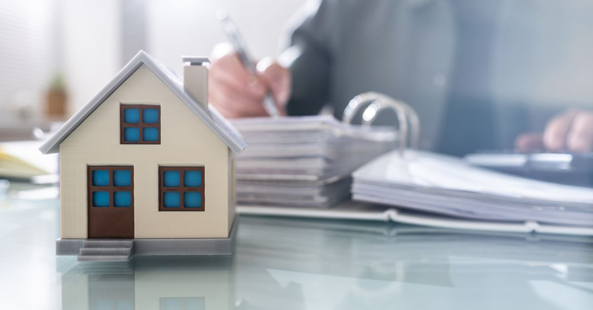 Image of a person filling out paperwork with a small toy house nearby