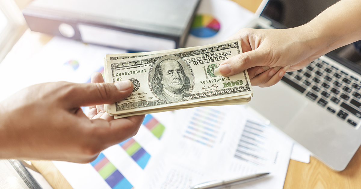 Image of a person paying another person with 100 dollar bills