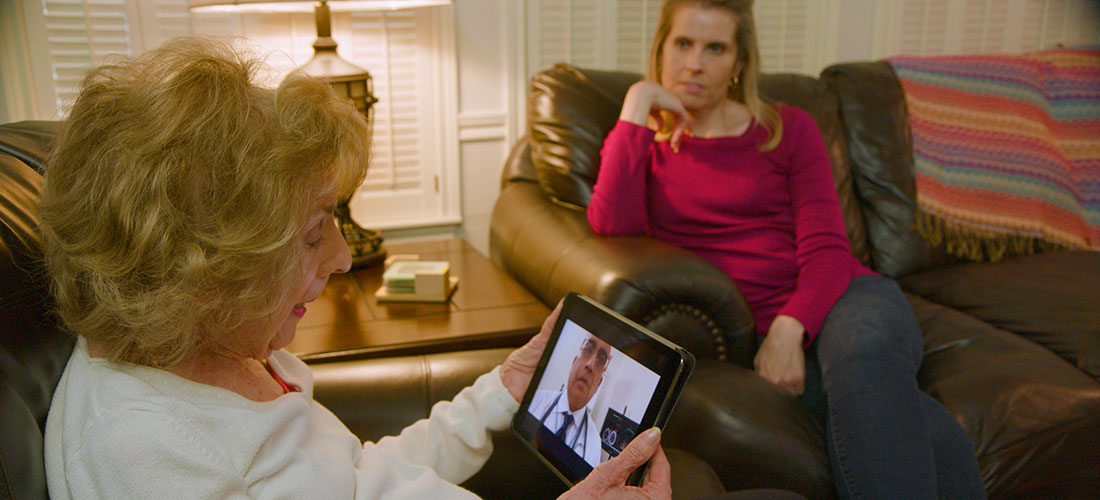 photo of an elderly woman patient receiving telehealth services on a video call with her doctor with adult daughter nearby