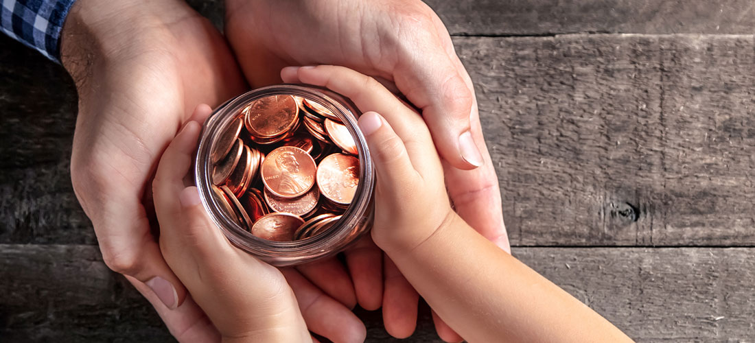 Photo showing the hands of an adult giving a jar of coins to the hands of a child.