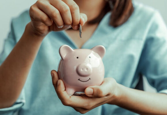 Image of a woman holding a smiling piggy bank, and she is adding a coin